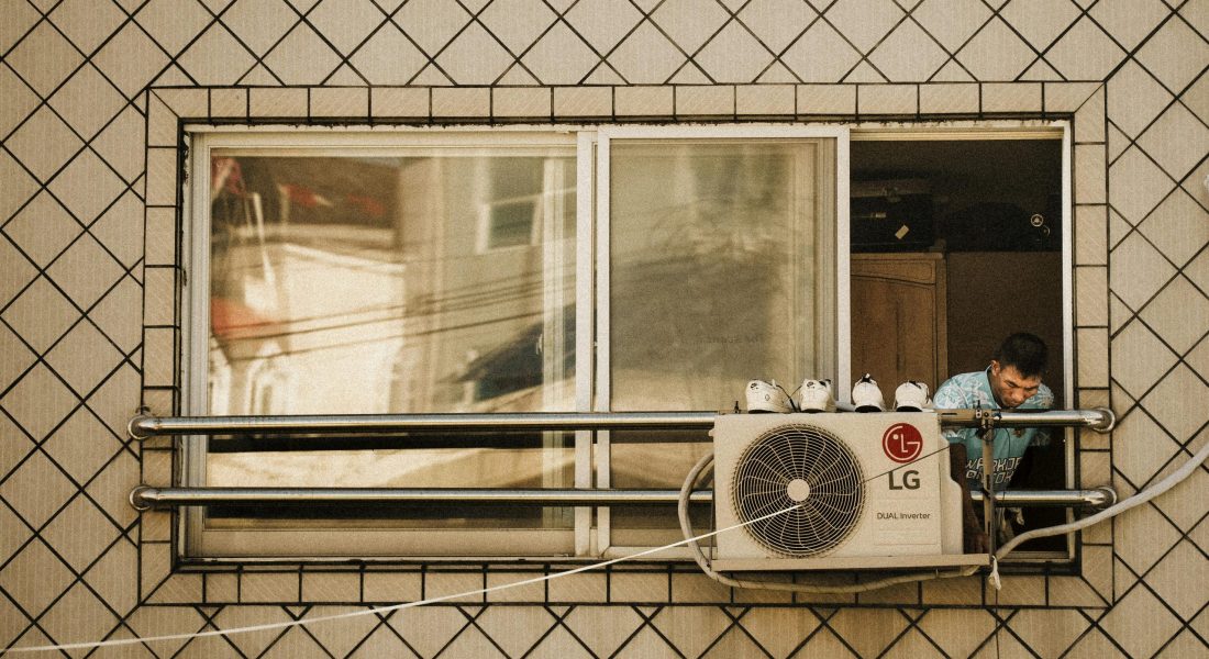 Man looks outside a window with an LG air conditioner unit visible, creating a reflective effect.